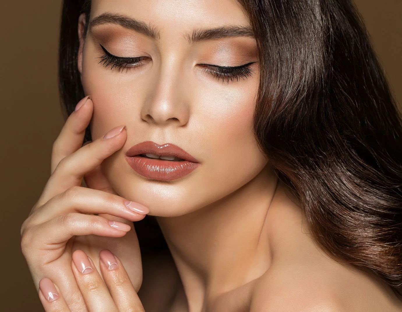 a woman with long brown hair touching the side of her face and eyes looking down