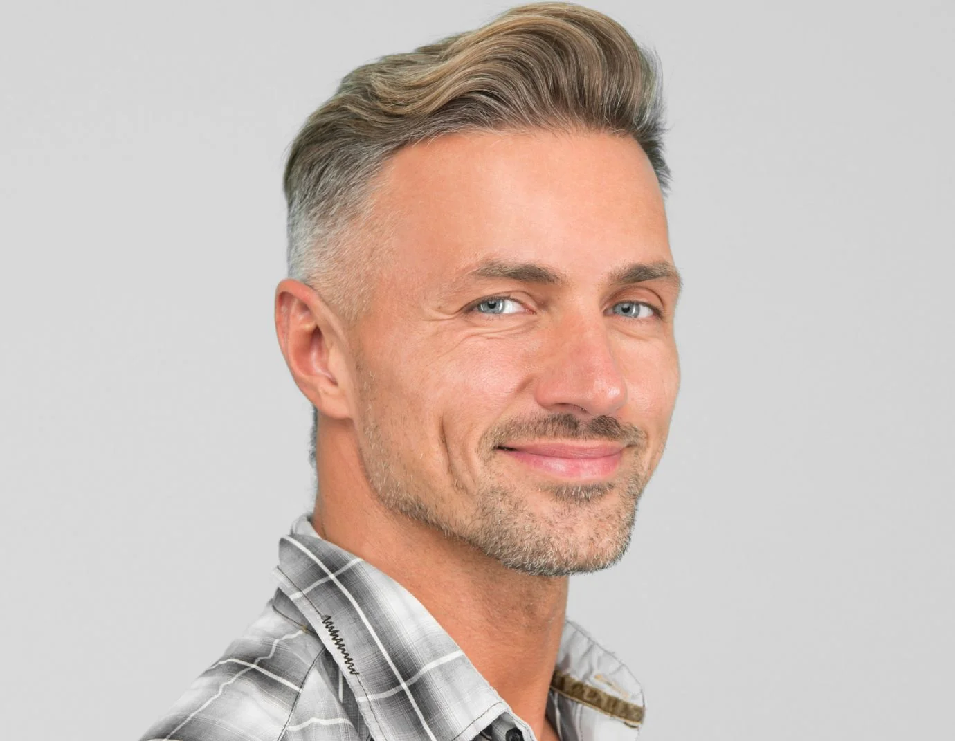 a man with blue grey eyes and wearing a flannel dress shirt against a grey background