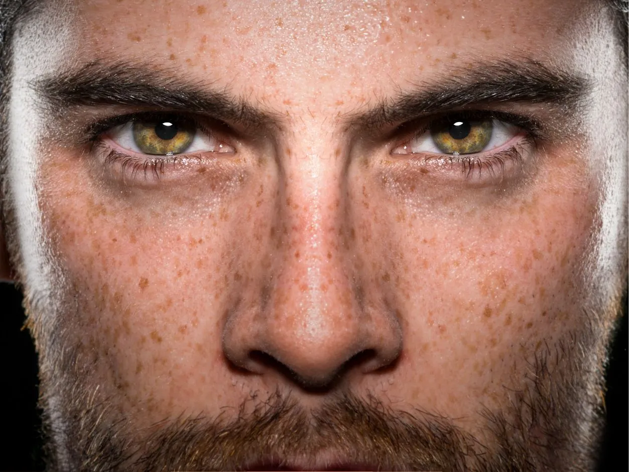 a close up shot of a man with a bearn, green eyes, freckles on his face and nose